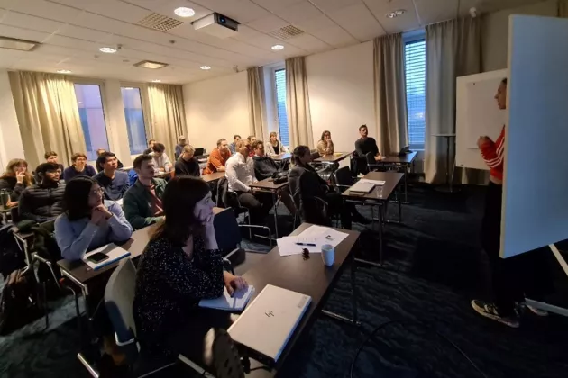 A room filled with listening people to a talk. Photo.