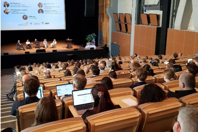 A large audience watching people in a panel on a stage