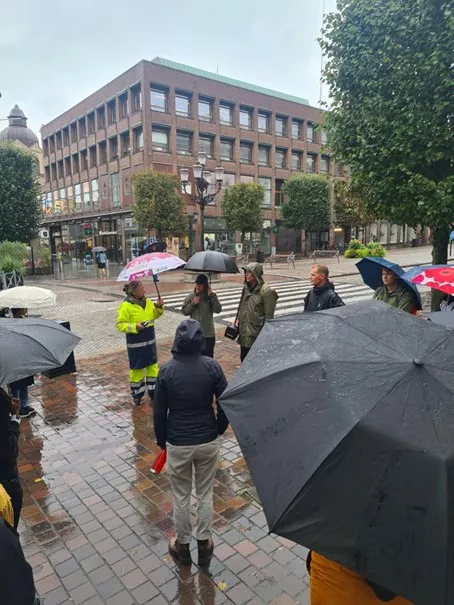 A person in yellow in urban setting with people around with umbrella. Photo.